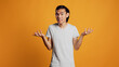 Clueless young person doing i dont know sign in studio, acting uncertain and unsure about answer to question. Asian guy being carefree and casual, acting doubtful over orange backdrop.