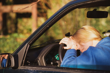Wall Mural - Tired woman driving a car. A middle-aged woman in her forties leaned over the steering wheel of a car. Fatigue, exhaustion, rest during the trip.