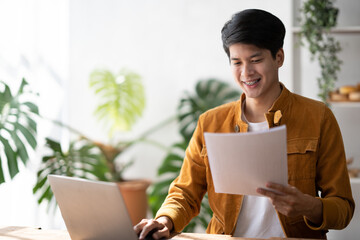 Smiling Asian man working on laptop in modern office space.