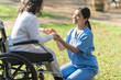 © NanSan - Young asian care helper with asia elderly woman on wheelchair relax together park outdoors to help and encourage and rest your mind with green nature. hold hands to encourage