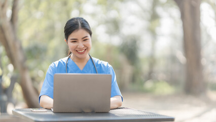 Asian female nurse working outdoor video call with patient online on laptop at desk in park.