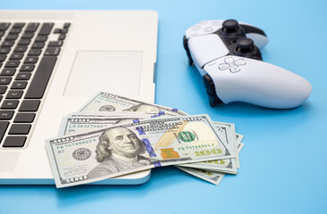 Wall Mural - Money, gamepad and laptop close-up on a blue background, the concept of gambling addiction.