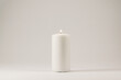 A lighted white wax candle burning isolated on white background with low light shadow.