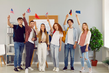 Young people who take part in university exchange program meet and make friends of different nationalities. Happy cheerful joyful international students standing together, holding up flags and smiling