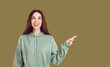 Enthusiastic joyful surprised woman introduce incredible offer pointing finger to right on copy space. Portrait of young caucasian woman in casual hoodie who presents or advertises on khaki background