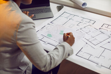 Female architect sitting at her office desk and working with blueprints, cadastral maps and city plans. Young African American woman studying information and developing a new architectural project