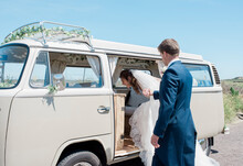 Groom Helping Bride Get Into A Camper Van On Their Wedding Day