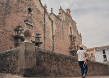 Tourist Girl Walking In Front Of An Old Stone Church In A Village In Spain