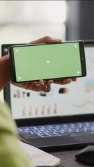 Poster - Vertical video: Woman looking at horizontal display with greenscreen in agency office, working with blank mockup template on smartphone. Young worker using isolated chroma key in coworking space.