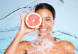 Beauty, skin care and woman portrait with a grapefruit for healthy skin and diet on blue background. Face of aesthetic model person water splash and fruit for sustainable facial health and wellness