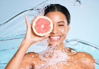 Wall Mural - Beauty, skin care and woman portrait with a grapefruit for healthy skin and diet on blue background. Face of aesthetic model person water splash and fruit for sustainable facial health and wellness