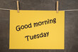 Napis Good morning Tuesday na wiszącej żółtej kartce na ciemnym tle