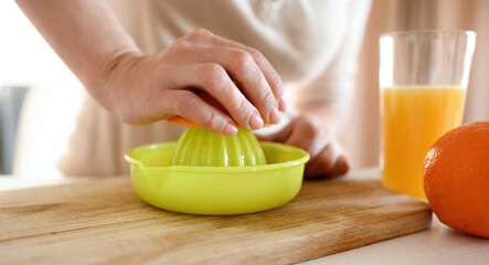 Poster - Girl hand squeeze ripe orange to manual extractor for making natural juice at kitchen. Woman preparing tropical fruit drink at home