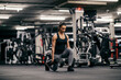 © dusanpetkovic1 - A muscular sportswoman is lifting dumbbells and doing lunges in a gym.
