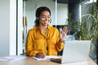 © Prostock-studio - Portrait of happy black businesswoman waving hello at webcamera, using laptop while working in office interior