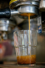 Close-up Of Espresso Dripping From A Bottomless Portafilter Into Glass Cup