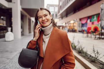 Cute brunette woman in brown coat talking on the phone in the city