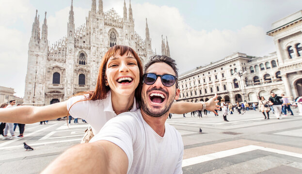 happy couple taking selfie in front of duomo cathedral in milan, lombardia - two tourists having fun