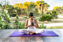 Calm Woman Meditating In Yoga Pose Against Plants