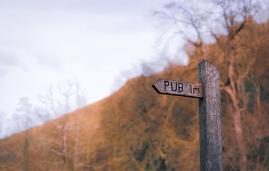 Old fashioned rustic wooden traditional pub signpost, on a nature walking footpath in the typical British countryside in Autumn, Derbyshire, England, Great Britain