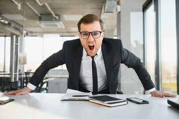 Wall Mural - Angry businessman sitting at his desk and screaming at his employees.