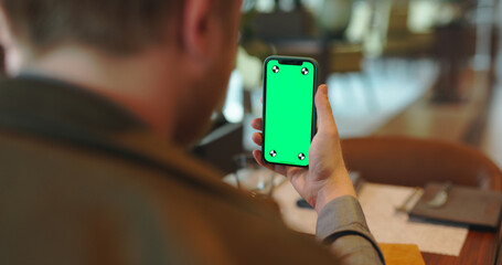 Wall Mural - Hands holding smartphone with green screen. man having a video chat on a phone. Guy talking in online conference via internet in cafe 