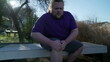 © Marco - Person suffering from knee pain sitting at bench outdoors. One overweight caucasian male person having physical injury