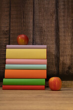 Stack Or Column Of Colored Books With Two Apples With Dark Wood Background And Light Wood Table Vertical Photo With Text Space