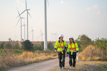 Two engineer or technician man and woman workers walk along the road far from windmill or wind turbine and talk together after finish work.