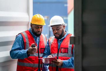 Portrait of Two African Engineer or foreman wears PPE checking container storage with cargo container background at sunset. Logistics global import or export shipping industrial concept.