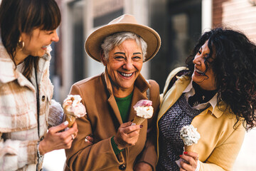 group of happy women eating ice cream outdoors at city urban street- three older mature friends girl