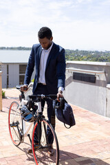 Wall Mural - African american businessman wearing suit and cycling to work with bag