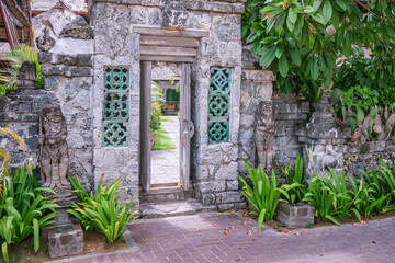 Open old wooden entry doors in stone wall with two traditional balinesian guard statues, street photo