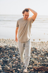 Wall Mural - Young adult teenager standing on the beach in a t-shirt and jeans with his hands in his hair