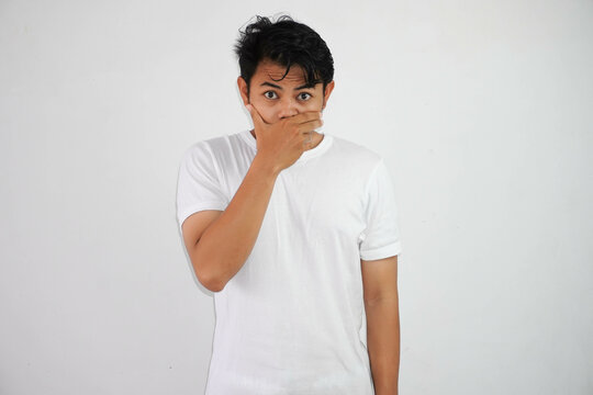 Portrait of scared young Asian man covering mouth with hands wearing white t shirt isolated on white background