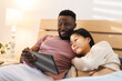 © Wavebreak Media - Happy diverse couple lying in bed and using tablet