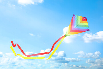 Bright striped rainbow kite flying in blue sky on sunny day