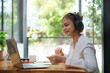 © wattana - Pretty young woman in headphones chatting in social networks, studying online remotely on laptop.