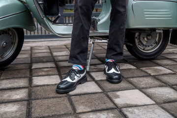 Wall Mural - These hand-made black-and-white wingtip shoes with loafers sole made from genuine leather are being worn to hang out with an old green Vespa	