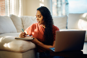 Wall Mural - Black female student takes notes while e-learning at home.