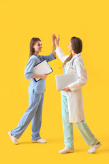 Wall Mural - Female doctor and intern giving each other high-five on yellow background