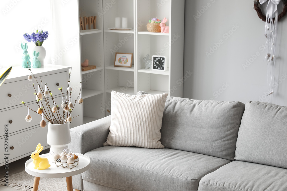 Vase with tree branches, Easter eggs and rabbit on table in interior of living room