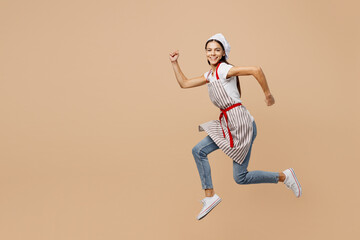 Full body side view smiling happy fun young housewife housekeeper chef baker latin woman wear apron toque hat run fast look camera isolated on plain pastel light beige background. Cook food concept.