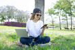 © Cavan Images - Front view of a happy student girl working with a laptop and smartphone in a green park of an university campus