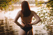 © Cavan Images - Back view of woman taking off her bikini top while standing in lake