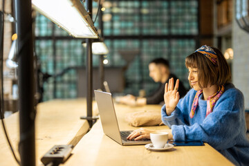 Wall Mural - Young stylish woman works on laptop while sitting by shared table with a coffee drink at modern cafe. Concept of remote work from public place, digital freelance and modern lifestyle