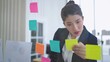 © M Stocker - Asian businesswoman using sticky paper notes to share idea on glass wall in office