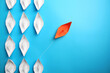 Orange paper boat floating away from others on light blue background, flat lay with space for text. Uniqueness concept