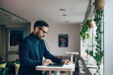 Businessman standing in the office, using a laptop.