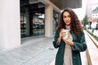 © fotofabrika - Young and cheerful woman walking with coffee cup through the city